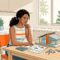 A homebuyer reviews plans beside a house model, calculator, papers, and keys at a bright kitchen table.