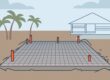 A concrete home foundation with reinforcement mesh, plumbing stubs, and palm trees nearby.